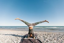 Afrikanisch-amerikanische junge Frau in Yoga-Kopfstand-Haltung vor dem Hintergrund der ruhigen See an sonnigen Tagen — Stockfoto