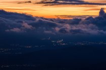 Landscape of hazy remote city lights in terrain under fluffy dark clouds with sunset sky — Stock Photo