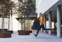 Trendy man in casual outfit looking at camera while running outside modern building — Stock Photo
