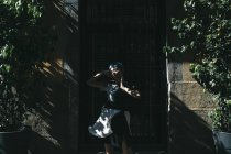 Junge Frau in futuristischem Kleid steht im Sonnenlicht auf der Straße vor altem Gebäude — Stockfoto