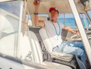 Alter Mann mit Mütze am Steuer und Kontrollleuchten leeren Küstenbereich bei hellem Tag — Stockfoto