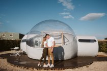 Side view of passionate man holding and kissing young woman while standing in front of romantic transparent glamping — Stock Photo