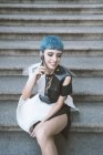 Сверху молодая женщина с короткими голубыми волосами и в модном футуристическом платье с телефоном на улице — стоковое фото