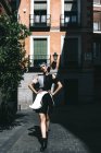 Jeune femme en robe futuriste debout avec les mains à la taille sur la rue contre le vieux bâtiment à la lumière du soleil — Photo de stock