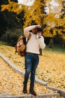 Красивый молодой фотограф, стоящий в осеннем парке и фотографирующийся с камерой — стоковое фото