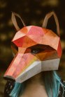 Anonymous female in paper fox mask covering full head looking away and standing on background with stack of logs. Concept of negative human impact on wildlife habitat — Stock Photo