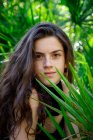 Portrait of smiling brunette young woman sitting in tropical green bushes — Stock Photo