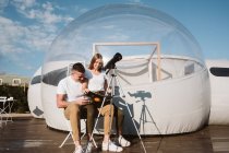 Elegante donna seduta sul grembo del fidanzato e la lettura dal telescopio al cielo vicino bolla hotel — Foto stock