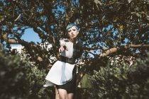 Знизу молода жінка в футуристичному одязі дивиться на камеру, стоячи біля дерев у розмитому стані — стокове фото