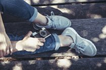 Зверху схрещені ноги в зручних кросівок і фотоапарат на дерев'яній лавці в яскравий сонячний день — стокове фото