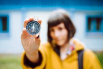 Cheerful blur young woman holding retro compass near face while standing on blurred background of countryside house — Stock Photo