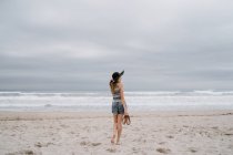 Vista posteriore di donna attraente in cappello nero godendo vista pittoresca dell'oceano — Foto stock