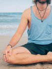 Abgeschnittenes Bild eines sportlichen bärtigen Mannes, der an der ruhigen Küste trainiert und Yoga-Asana gegen blaues Meer und Himmel macht — Stockfoto