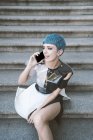 D'en haut de la jeune femme aux cheveux bleus courts et en robe futuriste tendance avec téléphone sur les marches de la rue — Photo de stock