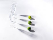 Ombre contrastanti da bicchieri d'acqua e lime verdi maturi su sfondo bianco — Foto stock
