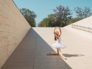 Ballerina performing with raising hands and stretching legs outside in bright sunny day — Stock Photo