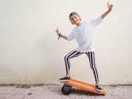 Stylish cute boy in trendy clothes performing trick on bright board and looking at camera on white background — Stock Photo