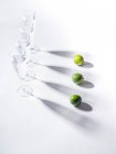 Ombres contrastées de verres d'eau et de limes mûres vertes sur fond blanc — Photo de stock