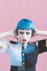 Молода жінка в модному альтернативному платті торкається короткого синього волосся і дивиться на камеру, стоячи на рожевій стіні на вулиці міста — стокове фото