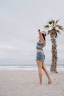 Mulher atraente vestindo top e shorts dançando na praia de areia com chapéu preto — Fotografia de Stock