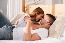 Joven pareja romántica en camisetas blancas y jeans acostados y abrazados en el dormitorio de glamping - foto de stock