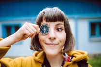 Cheerful young woman crossing eyes and holding retro compass near face while standing on blurred background of countryside house — Stock Photo