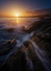 Vue pittoresque de l'eau de mer propre roulant et éclaboussant près des pierres rugueuses pendant le coucher du soleil merveilleux — Photo de stock
