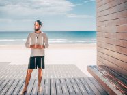 Adult bearded man standing relaxed resting on wooden pier by seashore looking away — Stock Photo