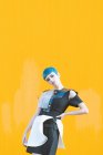 Junge Frau im trendigen futuristischen Kleid blickt in die Kamera, während sie auf Knien auf dem Bürgersteig vor einer leuchtend gelben Wand steht — Stockfoto