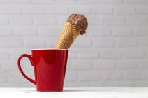 Chocolate ice cream cone in red cup against white brick wall — Stock Photo
