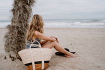 Side view of young beautiful blonde woman sitting down on beach and looking away — Stock Photo