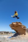 Експресивна жінка робить екстремальний трюк над великим скелястим каменем у дикій пустелі на фоні блакитного неба — стокове фото