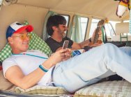 Vue latérale des hommes souriants textos et la navigation avec des gadgets dans la bande-annonce confortable mignon — Photo de stock
