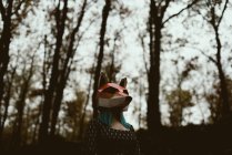 Mujer anónima en máscara de zorro de papel caminando en misterioso bosque otoñal en tiempo nublado. Concepto de protección del hábitat de vida silvestre - foto de stock
