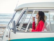 Vista laterale della giovane donna che colora le labbra seduta sul sedile anteriore dell'auto al mare — Foto stock