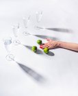 Жіноча рука з зеленими стиглими лімітами біля прозорих склянок води на білому тлі — стокове фото
