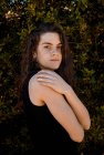 Porträt einer jungen Frau, die vor Buschhintergrund steht und in die Kamera blickt — Stockfoto