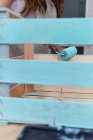 Nahaufnahme einer Frau, die Holzkiste in blauer Farbe mit Walze bemalt — Stockfoto