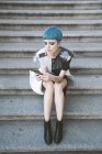 Сверху молодая женщина с короткими голубыми волосами и в модном футуристическом платье слушает музыку с телефоном на улице — стоковое фото