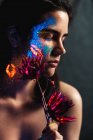 Portrait of beautiful young woman with closed eyes covered with luminous paint on face holding a flower — Stock Photo