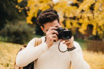 Bel giovane fotografo in piedi nel parco autunnale e scattare foto con la macchina fotografica — Foto stock