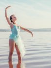 Ballerina tritt bei strahlendem Sonnenschein mit erhobenen Händen im welligen Wasser auf — Stockfoto