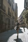 Mujer joven en vestido futurista de pie en la calle contra el viejo edificio a la luz del sol - foto de stock