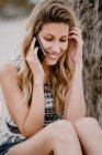 Junge attraktive Frau mit langen Haaren entspannt sich am Strand und telefoniert an Sommertagen mit dem Handy — Stockfoto