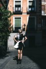 Jovem mulher em vestido futurista de pé com as mãos na cintura na rua contra o velho edifício à luz do sol — Fotografia de Stock