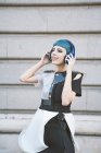 Зверху молода жінка з коротким блакитним волоссям і в модному футуристичному платті слухати музику з телефоном на вулицях — стокове фото