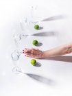 Жіноча рука з зеленими стиглими лімітами біля прозорих склянок води на білому тлі — стокове фото