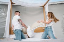 Allegro giovane coppia divertirsi durante la lotta cuscino sul letto in tenda grande con tetto trasparente — Foto stock