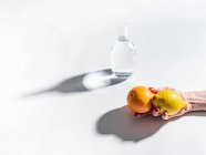 Nahaufnahme einer weiblichen Hand, die reife Orangen und Zitronen in der Nähe eines klaren Wasserglases auf weißem Hintergrund hält — Stockfoto