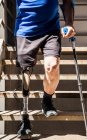 Неузнаваемый человек, ампутированный костылями, испытывает свой новый протез ноги, спускаясь по лестнице — стоковое фото